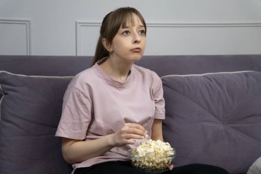 Sıkıcı genç bir kadın evinde rahat bir kanepede oturmuş, sıkıcı bir film izlerken cam kaseden patlamış mısır yiyordu, akşam eğlencesi seçiminden memnun değildi.