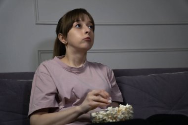 Genç bir kadın geceleri rahat bir şekilde kanepede oturup televizyon izlerken patlamış mısırın tadını çıkarıyor. Kendini eğlenceye kaptırırken düşünceli bir yüz ifadesi sergiliyor.