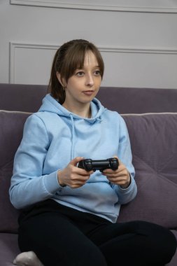 Genç bir kadın, elinde joystickle rahat bir koltukta oturup video oyunları oynuyor, evde boş zamanlarının tadını çıkarıyor, sanal mücadeleyi kazanmaya odaklanıyor. Dikey fotoğraf
