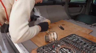 Arabanın bagajında çalışan siyah eldivenli erkek teknisyen, yeni bir yakıt pompası modülü ve seviye sensörünü profesyonel soket anahtarı olan bir alet çantasının yanında monte ediyor.