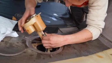 Otomotiv teknisyeni garajdaki tamirat sırasında modern bir aracın benzin deposuna dikkatlice yeni bir yakıt pompası monte ederek karmaşık bir bakım prosedürü sergiliyor.