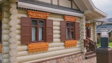 Süslü ahşap pencere çerçeveleri ve kahverengi kepenklerin yer aldığı, kırsal halk mimarisi ve klasik kırsal yapı tarzının sergilendiği geleneksel ahşap kulübe cephesi.