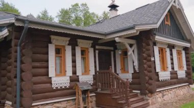 Beyaz oymalı ahşap pencere çerçeveleri ve kepenkleri olan, çevresi yeşil ağaçlarla çevrili, kırsal bir kırsal alana kurulmuş, güzel bir şekilde hazırlanmış geleneksel Rus ahşap evi.