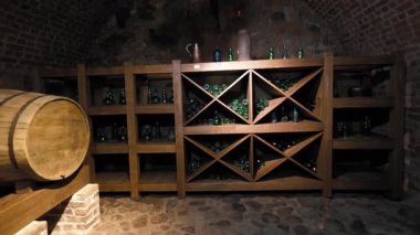 Otantik eski şarap mahzeni, kemerli tuğla duvarları ve taş zeminiyle, eski yeşil şişelerle dolu büyük bir ahşap raf ve yaşlanan alkollü içecekler için geleneksel meşe fıçısı.