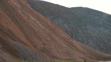 Büyük endüstriyel maden atığı yığını, kırmızı-kahverengi ve gri maddeler arasında katı bir zıtlık gösteriyor, görünür erozyon desenleri, gerçeküstü, insan yapımı bir manzara yaratıyor.