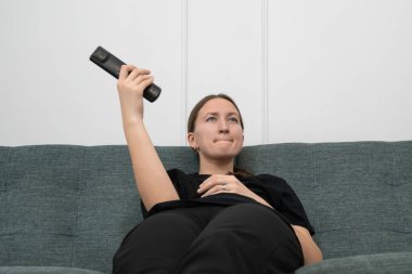 Genç bir kadın rahat bir şekilde kanepede uzanıyor. Uzaktan kumandayı havada tutuyor ve hafta sonu evde geçireceği dinlendirici bir hafta sonu boyunca televizyonda izleyecek ilginç bir şeyler arıyor.