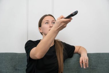 Genç bir kadın rahat bir kanepede dinleniyor, uzaktan kumandayla kanal değiştiriyor ve en sevdiği televizyon programlarının keyfini çıkarıyor.