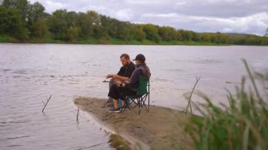 Genç çift birlikte kaliteli zaman geçiriyor, nehir kenarındaki sandalyelerde oturuyor ve oltalarını balık tutacakları bir gün için hazırlıyor, doğada sakin bir hafta sonu kaçamağının keyfini çıkarıyorlar.