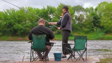 Romantik bir çift nehir kıyısında duruyor ve bulutlu bir günde dönen çubuklarla balık tutuyor, boş zamanlarının keyfini çıkarıyor ve doğada birlikte kaliteli zaman geçiriyorlar.