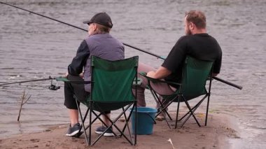 Rahatlamış erkek ve kadın huzurlu bir balık avının tadını çıkarıyorlar. Çubuk ve oltaları ile nehir kenarında oturuyorlar. Yaz tatilleri boyunca doğada sakin bir anı paylaşıyorlar.