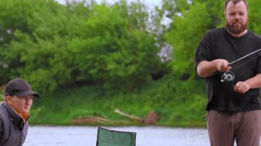 Rahatlamış erkek ve kadın huzurlu bir balık avının tadını çıkarıyorlar. Çubuk ve oltaları ile nehir kenarında oturuyorlar. Yaz tatilleri boyunca doğada sakin bir anı paylaşıyorlar.