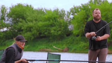 Rahatlamış erkek ve kadın huzurlu bir balık avının tadını çıkarıyorlar. Çubuk ve oltaları ile nehir kenarında oturuyorlar. Yaz tatilleri boyunca doğada sakin bir anı paylaşıyorlar.