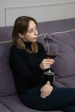 Kanepede oturmuş kırmızı şarap içen, üzgün ve bunalımlı, yalnızlık, depresyon ya da kırık kalp acısı çeken genç bir kadın. Dikey fotoğraf