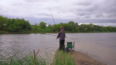 Birkaç erkek ve kadın kumlu nehir kıyısında dinlenmenin keyfini çıkarıyorlar: biri ayakta ve atış halatı, diğeri olta kamışı ile katlanır bir sandalyede oturuyor.