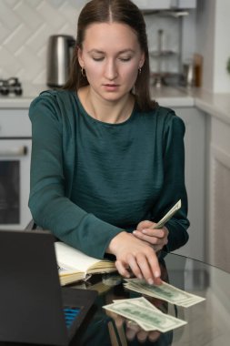 İş kadını ofisteki cam masada oturuyor, bize dolar banknotları sayıyor, yakınlarda dizüstü bilgisayarları ve defterleri var, ev finansmanlarını, bütçe hesaplarını veya hesaplama yatırımlarını yönetiyor.