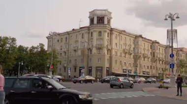 Minsk, Belarus - 13 Temmuz 2024: Şehir kavşağından geçen şehir trafiği Minsk, Belarus 'ta bir saat kulesi olan tarihi bir binanın önünde gündüz vakti bulutlu bir gökyüzünün altında