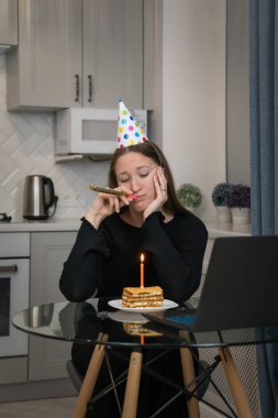 Üzgün kadın parti şapkası takıyor, internette doğum gününü kutlarken parti kornası çalıyor. Elinde bir dilim pasta ve mumla evde oturuyor, bilgisayarına bağlanıyor.