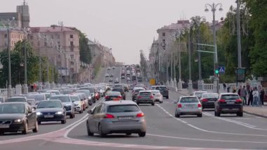 Minsk, Belarus - 13 Temmuz 2024: Yoğun araba akışı yoğun saatlerde Avrupa 'nın çok şeritli caddesinde ağır ağır ilerlerken, arka planda yürüyen yayalarla trafik sıkışıklığı yaratıyor