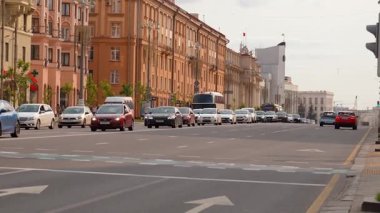 Minsk, Belarus - 13 Temmuz 2024: Şehir merkezinde tarihi binalarla dolu geniş, çok şeritli bir cadde boyunca arabalar ve otobüsler ilerlerken trafik ışıkları yeşilden kırmızıya dönüyor