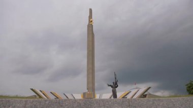 Minsk, Belarus - 13 Temmuz 2024: Belarus büyük vatansever savaş müzesi önünde anavatan heykeli bulunan Minsk kahraman şehri dikilitaş dramatik bulutlu gökyüzü altında, önemli bir dünya savaşı anısı.