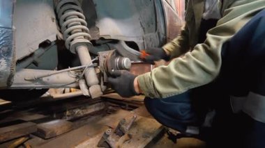 Profesyonel bir tamirci arabanın arka tekerleğinin fren diskini değiştiriyor. Merkezi tel fırçayla temizliyor ve düzenli bakım sırasında yeni bir disk takıyor.