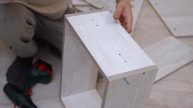 Evde yeni ahşap mobilyalar monte eden bir adamın elleri kablosuz tornavida kullanarak parçacık panellerini tek başına yenileme sırasında takıyor.