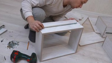 Aletler ve çeşitli parçalarla çevrili yeni dolap mobilyalarını monte ederken ahşap bir çekmecenin üzerine metal bir slayt rehberi yerleştiren odaklı tamirci.