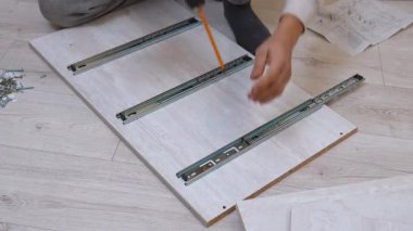 Erkek eller metal çekmeceleri takmak için kablosuz tornavida kullanıyor tahta bir tahtaya kayıyor ve talimatlara göre yeni mobilyaları kendi evlerinde dikkatlice monte ediyorlar.