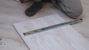 Profesyonel bir tamirci, elektrikli tornavidayla tahta bir panele metal slaytlar yerleştiriyor. Yeni ev mobilyalarını monte ederken donanımı dikkatlice ölçüyor ve vidalıyor.