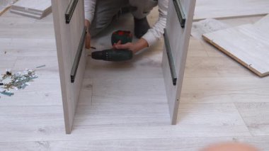Yeni bir ahşap dolap yapmak için kablosuz elektrikli tornavida kullanarak yerde konsantre bir adam var. Ev geliştirme projesi için parçaları dikkatlice birleştiriyor.