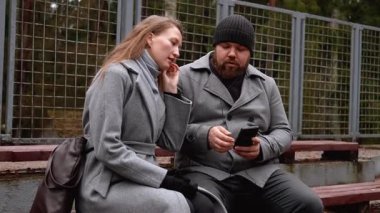 Gri ceketli genç bir adam ve bir kadın sonbahar parkında bankta oturuyorlar, kulaklıklarıyla müzik dinliyorlar ve birlikte romantik bir anın tadını çıkarıyorlar.