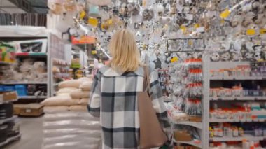 Sarı Saçlı Alışverişçi Kadın, büyük hırdavatçı dükkanında geziyor, yenileme, iç dekorasyon veya farklı ürünler arasında ev dekorasyonu arıyor.