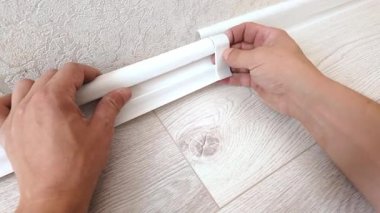 Erkek eller duvardaki iki parça kalıbı birleştirmek için beyaz plastik bir etek bağı kuruyor ve ev yenileme projesi sırasında döşeme kurulumunu tamamlıyor.