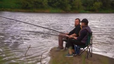 Bulutlu bir günde nehir kıyısında balık tutan genç bir çift. Birlikte vakit geçirmek. Nehir kenarında aile tatilleri.