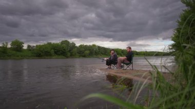 Bulutlu bir günde nehir kıyısında balık tutan genç bir çift. Birlikte vakit geçirmek. Nehir kenarında aile tatilleri.