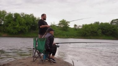 Sakin bir adam ve kadın nehir kenarındaki katlanan sandalyelerde oturur, sabırla olta kamışı tutar ve bir ısırık bekler, bulutlu bir günde birlikte sakin bir açık hava hobisinin keyfini çıkarırlar.