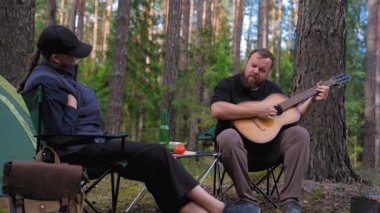 Genç bir çift, kamp alanında sakin bir akşamın tadını çıkarıyor. Sakallı bir adam bir kadın için akustik gitar çalıyor. Kamp sandalyelerinde çadırın yanında dinleniyor ve kamp ateşi yakıyor.