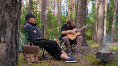 Genç bir çift, kamp alanında sakin bir akşamın tadını çıkarıyor. Sakallı bir adam bir kadın için akustik gitar çalıyor. Kamp sandalyelerinde çadırın yanında dinleniyor ve kamp ateşi yakıyor.