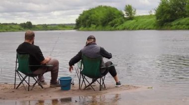 Genç bir adam ve kadın küçük kumlu bir adada katlanır sandalyelerde oturur, bulutlu bir günde nehirde oltayla balık tutar, birlikte huzurlu bir açık hava aktivitesinin keyfini çıkarırlar.