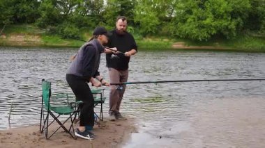 Mutlu yetişkin çift boş zamanlarını sakin bir nehir kıyısında balık tutarak geçiriyorlar. Kadın oturup huzur dolu doğanın tadını çıkarırken, erkek oltasını suya atıyor.