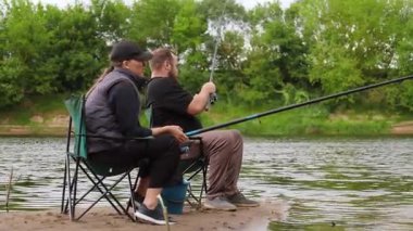 Kadın ve erkek birlikte sakin bir gün geçirmenin tadını çıkarıyorlar. Nehir kenarındaki katlanır sandalyelerde oturuyorlar. Çubukları suyun içinde.