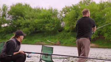 Bir erkek ve bir kadın, birlikte huzurlu bir gün geçirmenin tadını çıkarıyorlar. Nehir kenarındaki sandalyelerde oturuyorlar. Çubukları suya dökülmüş, yemyeşil ağaçlar ve sakin doğayla çevrili.