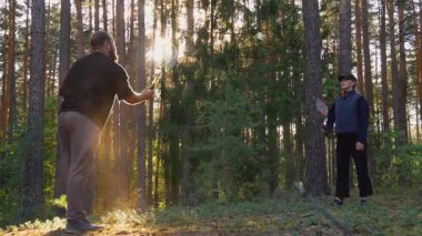 Bir çift adam ve bir kadın ağaçların arasından altın güneş ışığının doğduğu ve hareketlerini vurguladığı güzel bir çam ormanında badminton oynuyorlar.
