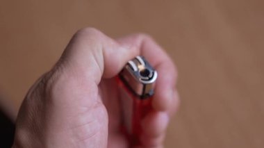 Kırmızı tek kullanımlık çakmağı yakmaya çalışan bir elin yakın çekimi. Çakmaktaşı birkaç kez kıvılcım saçar ama gaz yanmaz. Bu da arızalı ya da boş bir nesneyi temsil eder.