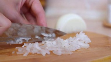 Profesyonel şefin elleri, ahşap bir kesme tahtasının üzerinde keskin bir bıçakla çiğ beyaz soğanı ince ince doğruyor. Lezzetli ve sağlıklı bir ev yemeği için malzemeler hazırlıyor.