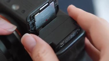 Medyayı depolamak için fotoğraf çekimi veya video çekimi başlatmadan önce fotoğrafçının ellerinin bataryayı profesyonel bir dijital aynasız kameranın yuvasına yerleştirmesi.