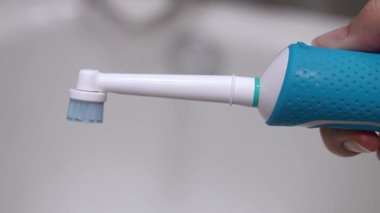 Çalışan bir elektrikli diş fırçasını tutan, dönen ve titreyen bir kafası olan, günlük ağız temizliği için modern teknolojiyi temsil eden ve banyoda etkili diş temizliği yapan bir elin yakın çekimi.