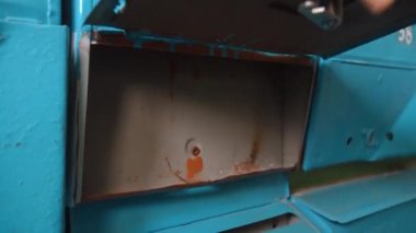 Bir insanın elinin eski, paslı, mavi bir posta kutusunun kilidine anahtar sokup boş kompartımanı açtığı ve sonra da bir apartmanda tekrar kapattığı yakın plan görüntüsü.