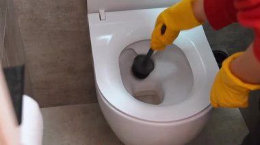 Profesyonel temizlikçi sarı koruyucu lastik eldivenlerle beyaz seramik bir klozeti siyah bir fırçayla yıkıyor ve fırçalıyordu.