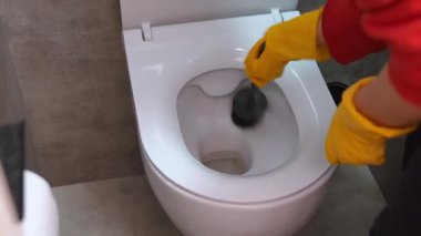 Profesyonel temizlikçi sarı koruyucu lastik eldivenlerle beyaz seramik bir klozeti siyah bir fırçayla yıkıyor ve fırçalıyordu.